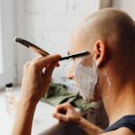 Person using a straight razor to shave a lathered cheek