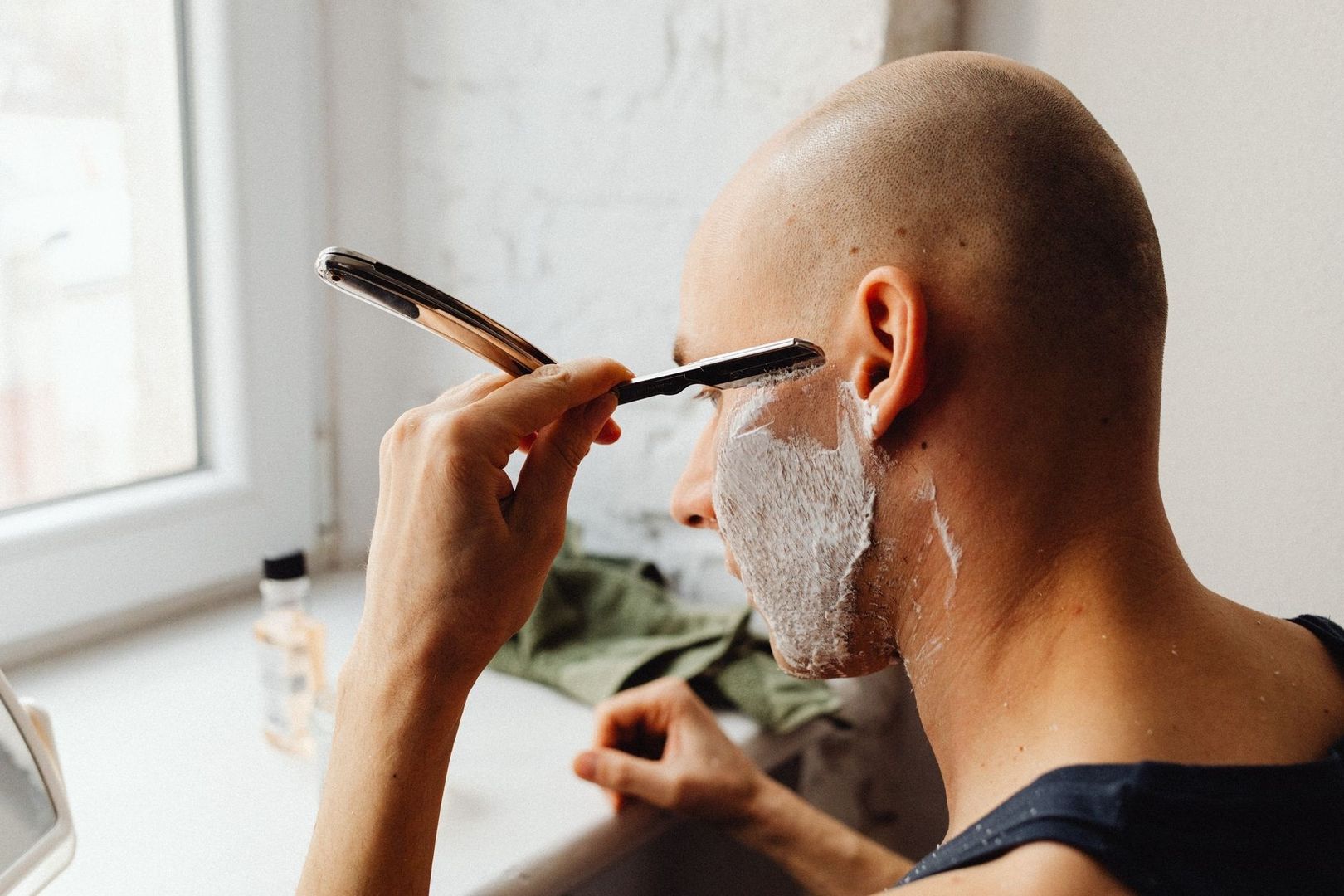 Person using a straight razor to shave a lathered cheek