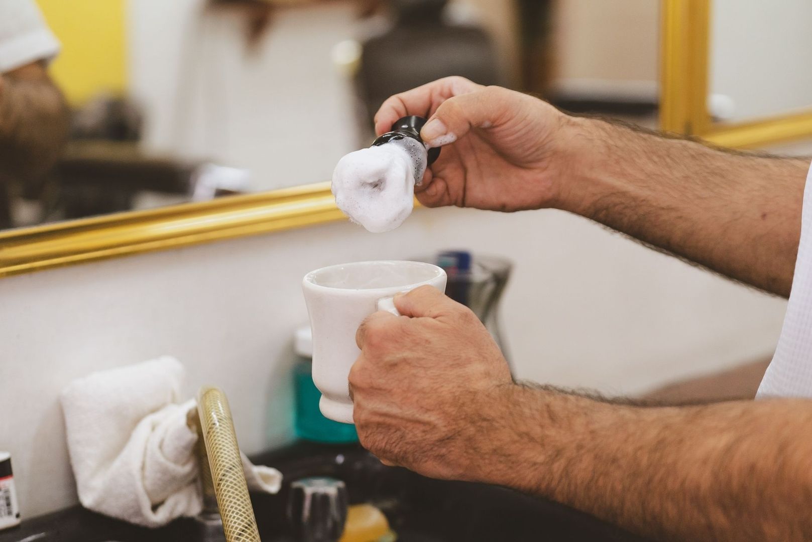Shaving brush covered in lather held above a white mug