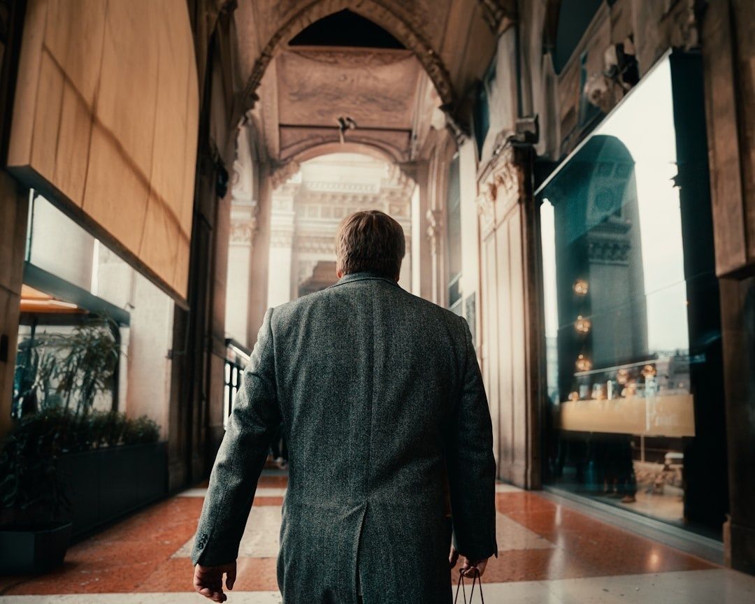 Man in a gray tweed jacket walking through an ornate city arcade